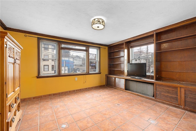 interior space with a textured ceiling, built in shelves, light tile patterned floors, and crown molding