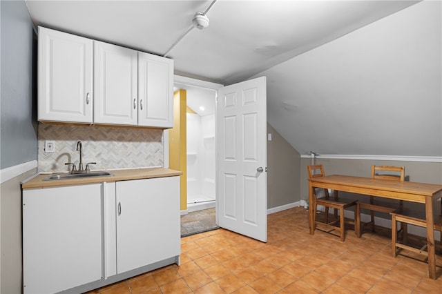 kitchen featuring white cabinets, tasteful backsplash, lofted ceiling, and sink