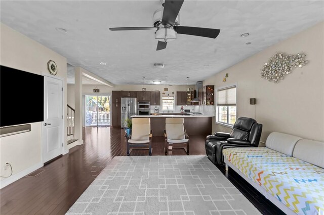 living room featuring plenty of natural light, ceiling fan, and dark wood-type flooring