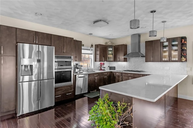 kitchen with pendant lighting, sink, wall chimney exhaust hood, dark brown cabinets, and stainless steel appliances