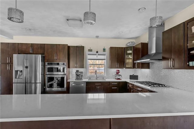 kitchen with decorative backsplash, appliances with stainless steel finishes, wall chimney exhaust hood, sink, and pendant lighting