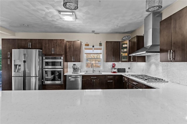 kitchen featuring backsplash, wall chimney range hood, sink, appliances with stainless steel finishes, and dark brown cabinetry