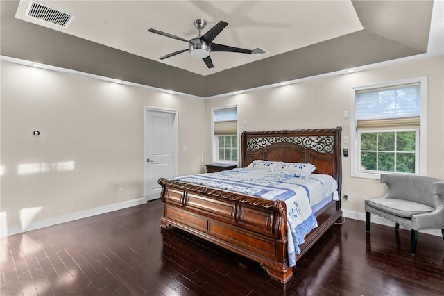 bedroom with dark hardwood / wood-style flooring, a raised ceiling, and ceiling fan