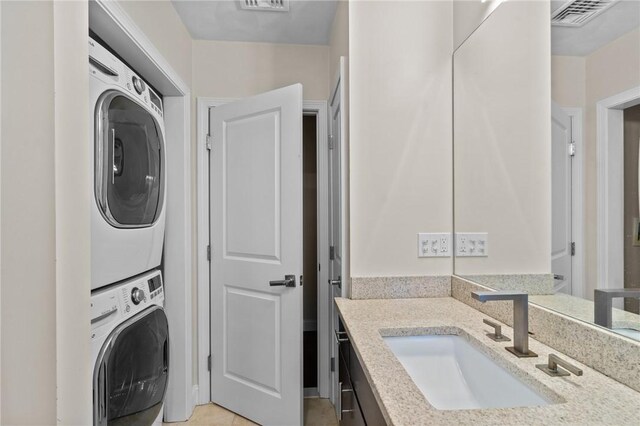 laundry area featuring stacked washer / dryer, sink, and light tile patterned floors