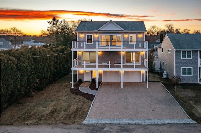 back house at dusk featuring a balcony, a garage, and a lawn