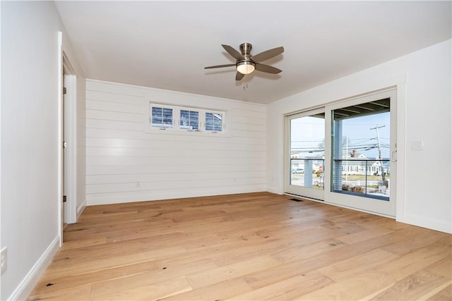 empty room featuring light hardwood / wood-style flooring, ceiling fan, and wooden walls