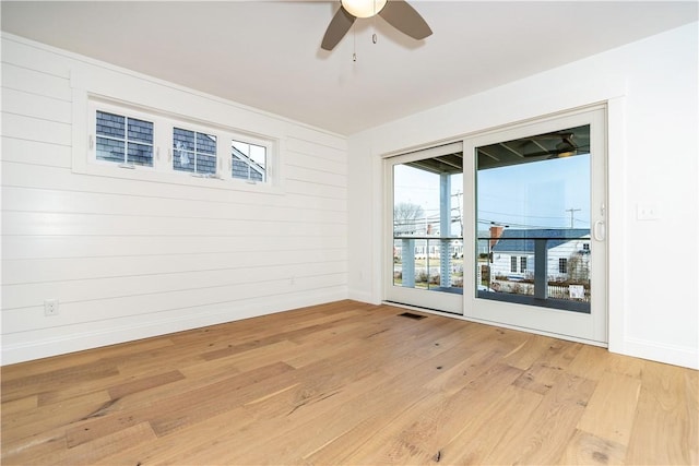 empty room with wood walls, ceiling fan, and light hardwood / wood-style floors