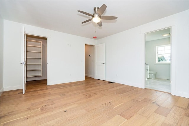 unfurnished bedroom featuring connected bathroom, a spacious closet, ceiling fan, light hardwood / wood-style flooring, and a closet