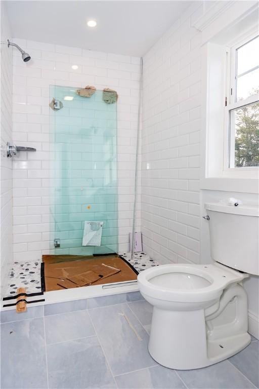 bathroom with tile patterned flooring, toilet, and a tile shower