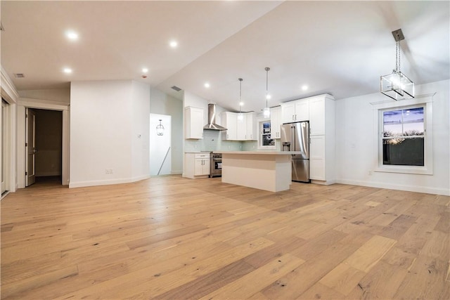 kitchen with a center island, wall chimney exhaust hood, decorative light fixtures, decorative backsplash, and appliances with stainless steel finishes