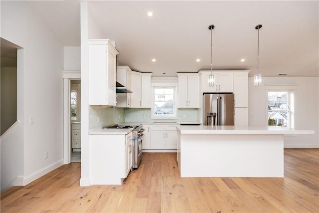 kitchen with high end appliances, white cabinets, ventilation hood, hanging light fixtures, and a kitchen island