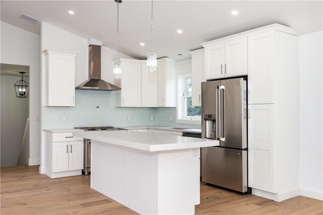 kitchen featuring pendant lighting, a center island, white cabinets, wall chimney range hood, and appliances with stainless steel finishes