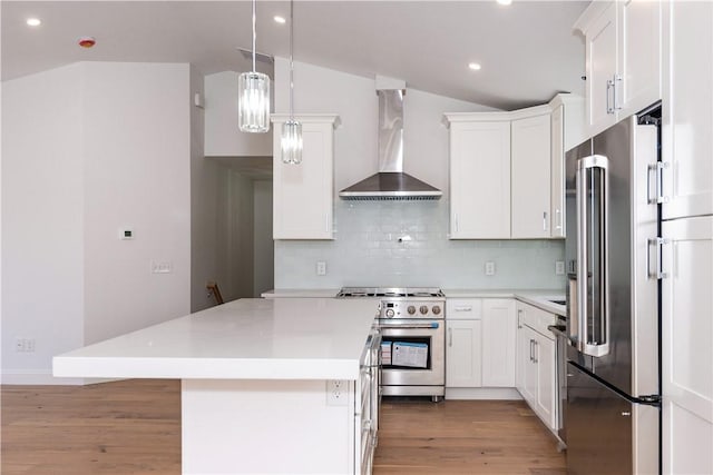 kitchen featuring decorative light fixtures, wall chimney exhaust hood, tasteful backsplash, premium appliances, and white cabinetry