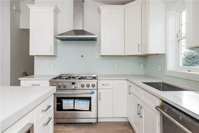 kitchen featuring white cabinetry, wall chimney range hood, tasteful backsplash, appliances with stainless steel finishes, and light wood-type flooring