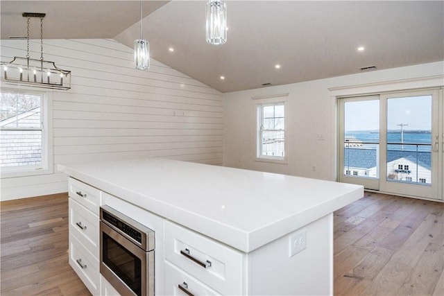 kitchen featuring decorative light fixtures, vaulted ceiling, a water view, and white cabinetry