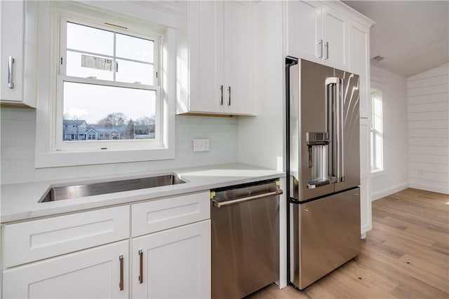 kitchen featuring white cabinetry, sink, light hardwood / wood-style floors, lofted ceiling, and appliances with stainless steel finishes