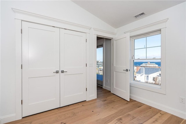 unfurnished bedroom featuring a closet, a water view, vaulted ceiling, and light hardwood / wood-style flooring