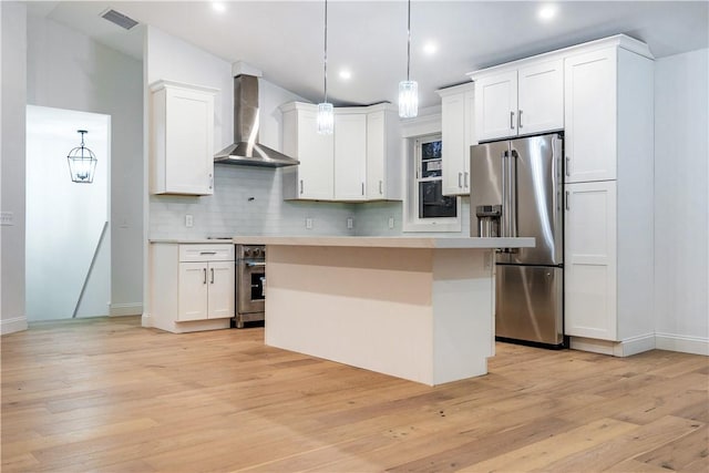 kitchen featuring white cabinetry, wall chimney range hood, decorative light fixtures, high quality fridge, and a kitchen island