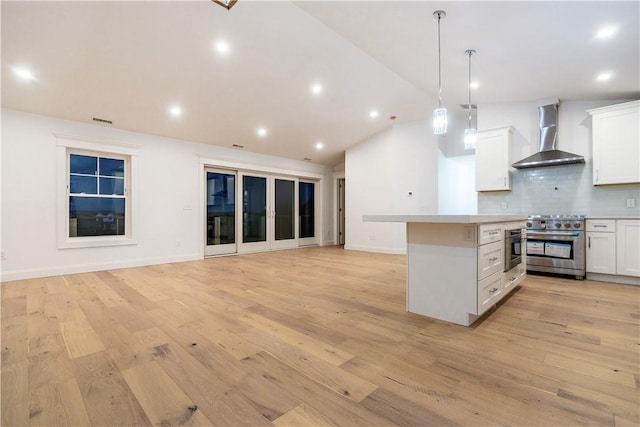 kitchen with pendant lighting, white cabinetry, high end range, and wall chimney range hood