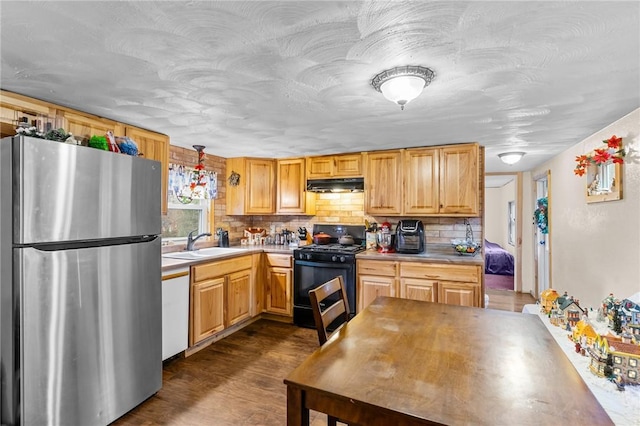 kitchen with black gas range, stainless steel refrigerator, sink, dark hardwood / wood-style floors, and decorative backsplash