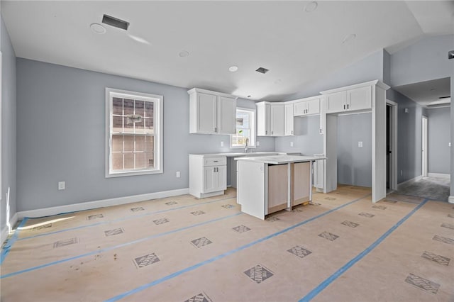 kitchen with white cabinets, vaulted ceiling, a kitchen island, and sink