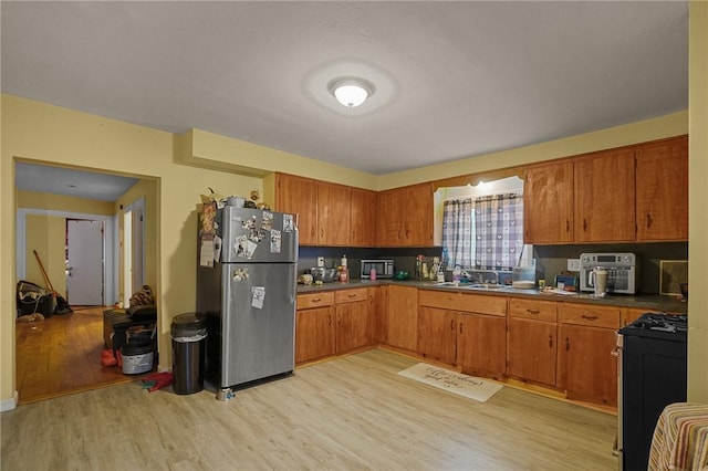 kitchen with stainless steel fridge, light hardwood / wood-style flooring, black range oven, and sink