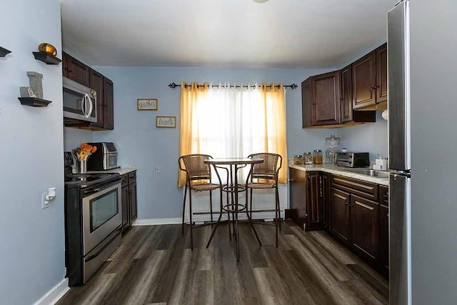 kitchen with appliances with stainless steel finishes, dark brown cabinets, dark wood-type flooring, sink, and a baseboard radiator