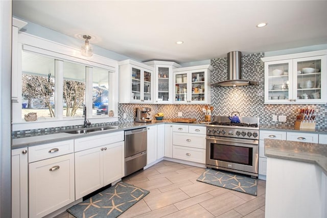 kitchen with wall chimney range hood, tasteful backsplash, appliances with stainless steel finishes, and a sink