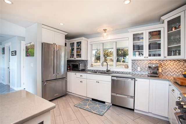 kitchen with glass insert cabinets, appliances with stainless steel finishes, a sink, white cabinetry, and backsplash