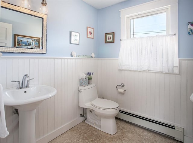 half bathroom with a baseboard radiator, wainscoting, and toilet