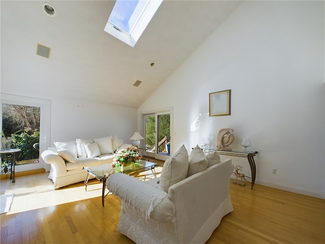 living room with light hardwood / wood-style floors, high vaulted ceiling, and a skylight