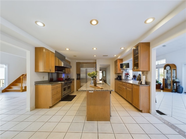 kitchen with a center island, wall chimney exhaust hood, high quality appliances, and light tile patterned flooring