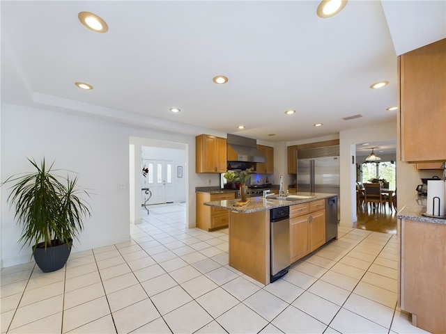 kitchen featuring wall chimney exhaust hood, sink, light tile patterned floors, and an island with sink