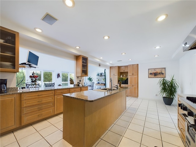 kitchen featuring a kitchen island with sink, stone counters, sink, stainless steel range, and light tile patterned flooring