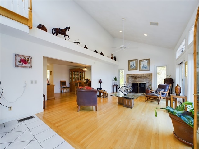 living room with a fireplace, a towering ceiling, light hardwood / wood-style floors, and ceiling fan