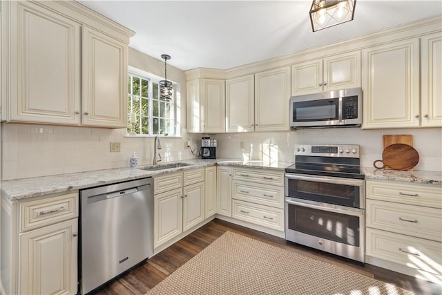 kitchen with cream cabinetry, appliances with stainless steel finishes, decorative light fixtures, and sink