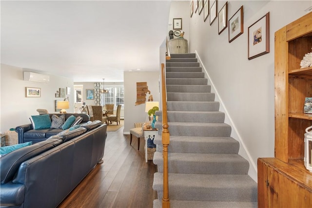 staircase featuring wood-type flooring, a wall mounted air conditioner, and a notable chandelier