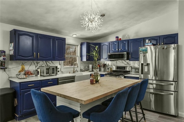 kitchen with hardwood / wood-style floors, lofted ceiling, an inviting chandelier, blue cabinets, and appliances with stainless steel finishes