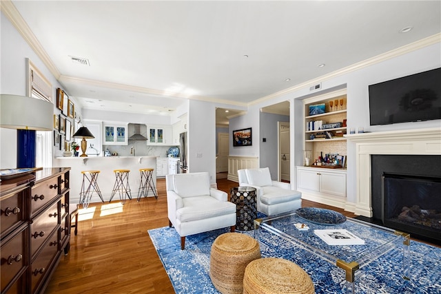 living room with built in features, hardwood / wood-style floors, and ornamental molding