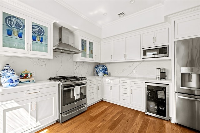 kitchen with white cabinetry, wall chimney exhaust hood, beverage cooler, decorative backsplash, and appliances with stainless steel finishes