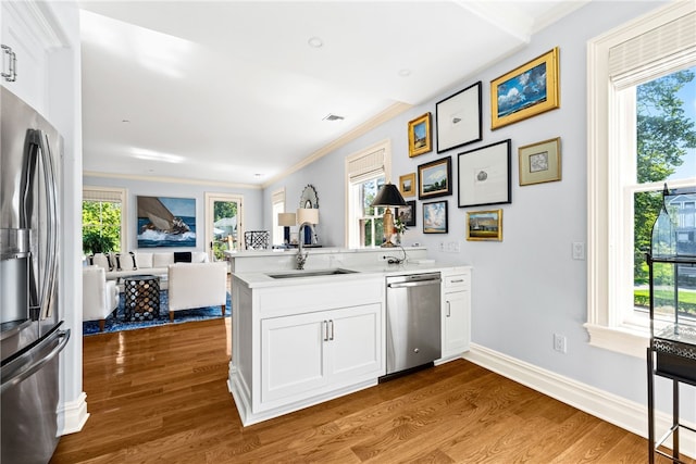 kitchen with sink, kitchen peninsula, hardwood / wood-style floors, white cabinets, and appliances with stainless steel finishes