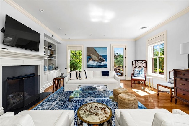 living room with built in shelves, crown molding, and wood-type flooring