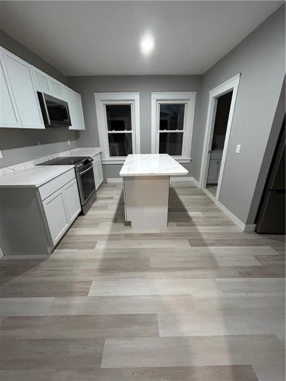 kitchen with appliances with stainless steel finishes, a center island, white cabinetry, and light stone counters