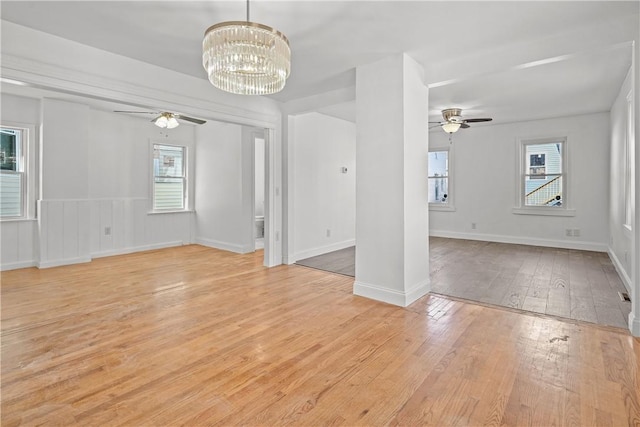 spare room with plenty of natural light, ceiling fan with notable chandelier, and light wood-type flooring