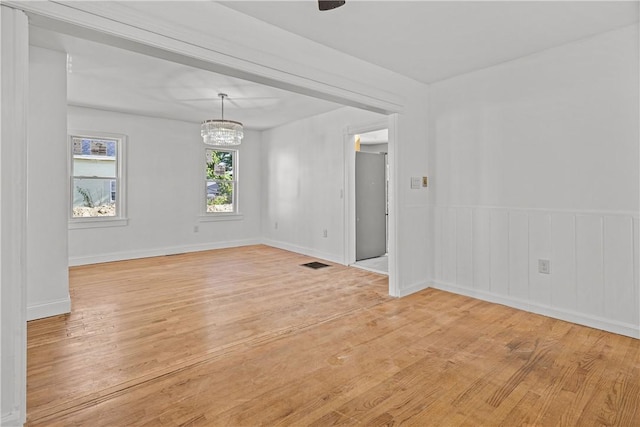 empty room featuring an inviting chandelier and light wood-type flooring