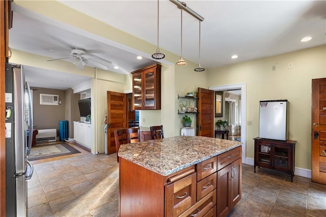 kitchen with light stone countertops, ceiling fan, stainless steel fridge, pendant lighting, and a kitchen island