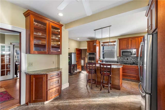 kitchen featuring appliances with stainless steel finishes, tasteful backsplash, light stone counters, decorative light fixtures, and a breakfast bar area