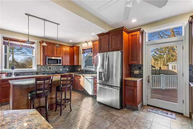 kitchen with sink, stainless steel appliances, tasteful backsplash, light stone counters, and pendant lighting