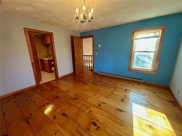 empty room featuring baseboard heating, a chandelier, sink, and light hardwood / wood-style floors