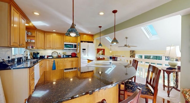 kitchen with decorative light fixtures, white appliances, ceiling fan, vaulted ceiling with skylight, and dark stone counters